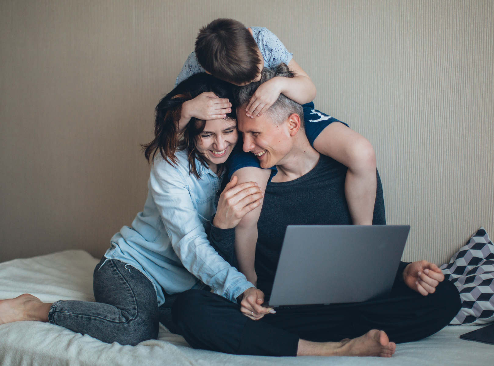 American Health Plans | Mom and Dad laughing on bed with child holding them both